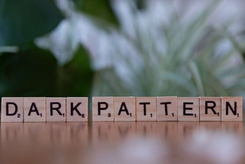Drewniane klocki z literami tworzące napis „DARK PATTERN” ustawione na drewnianym blacie.