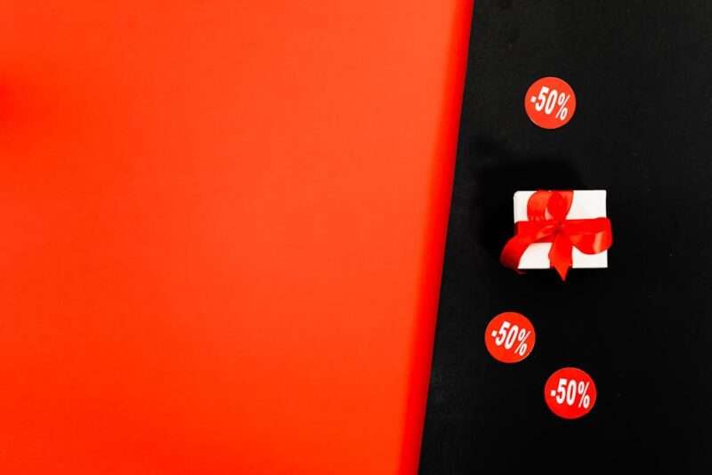 Białe pudełko z czerwoną kokardą i trzy naklejki z napisem -50%.