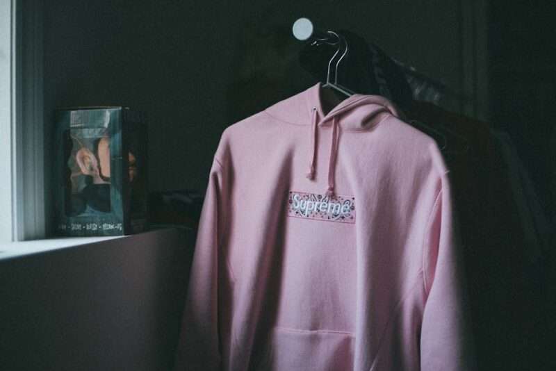 Różowa bluza z kapturem Supreme z motywem bandany wisząca na wieszaku.