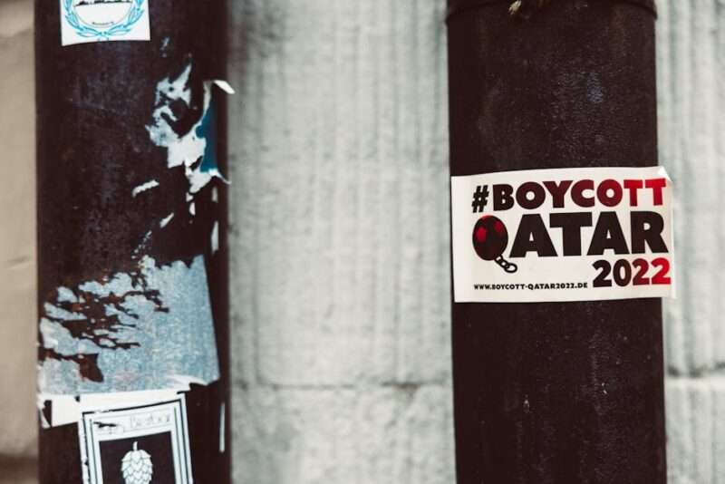 Naklejka z napisem #BOYCOTT QATAR 2022 na ciemnym, metalowym słupie.