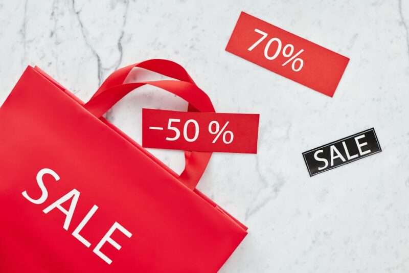 Czerwona torba zakupowa z napisami „SALE” oraz metkami z rabatami 70% i 50%.