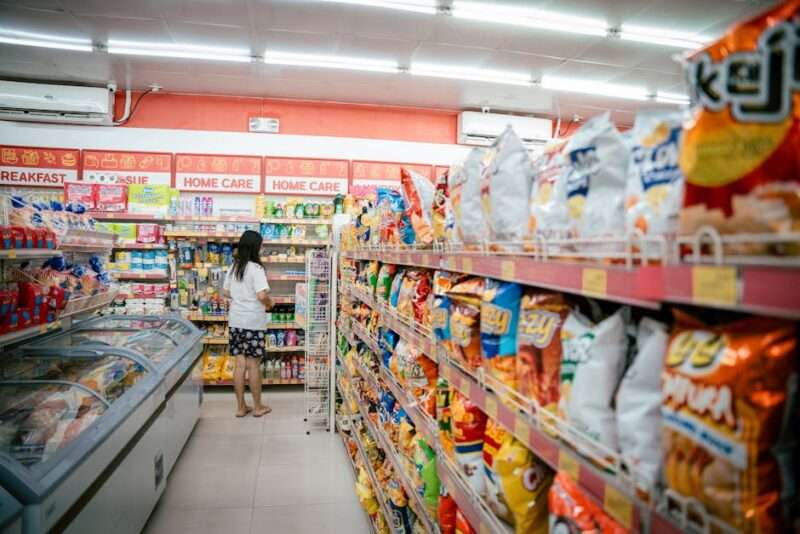Kobieta stojąca przy półkach z produktami chemicznymi w sklepie spożywczym.