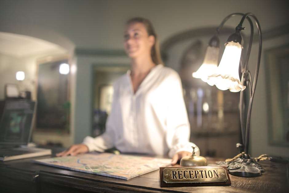 Recepcjonistka przy hotelowym biurku z mapą, dzwonkiem i lampą.