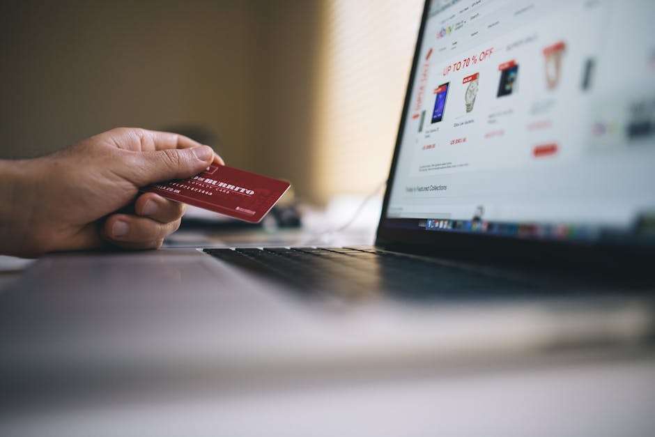 Dłoń trzymająca kartę lojalnościową obok otwartego laptopa z witryną zakupową.