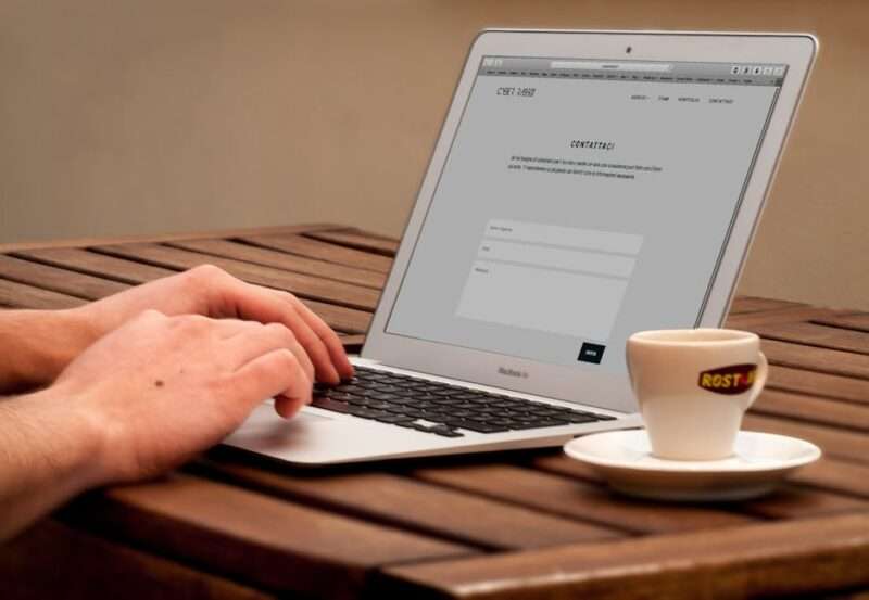 Osoba korzystająca z laptopa na drewnianym stole obok filiżanki kawy.